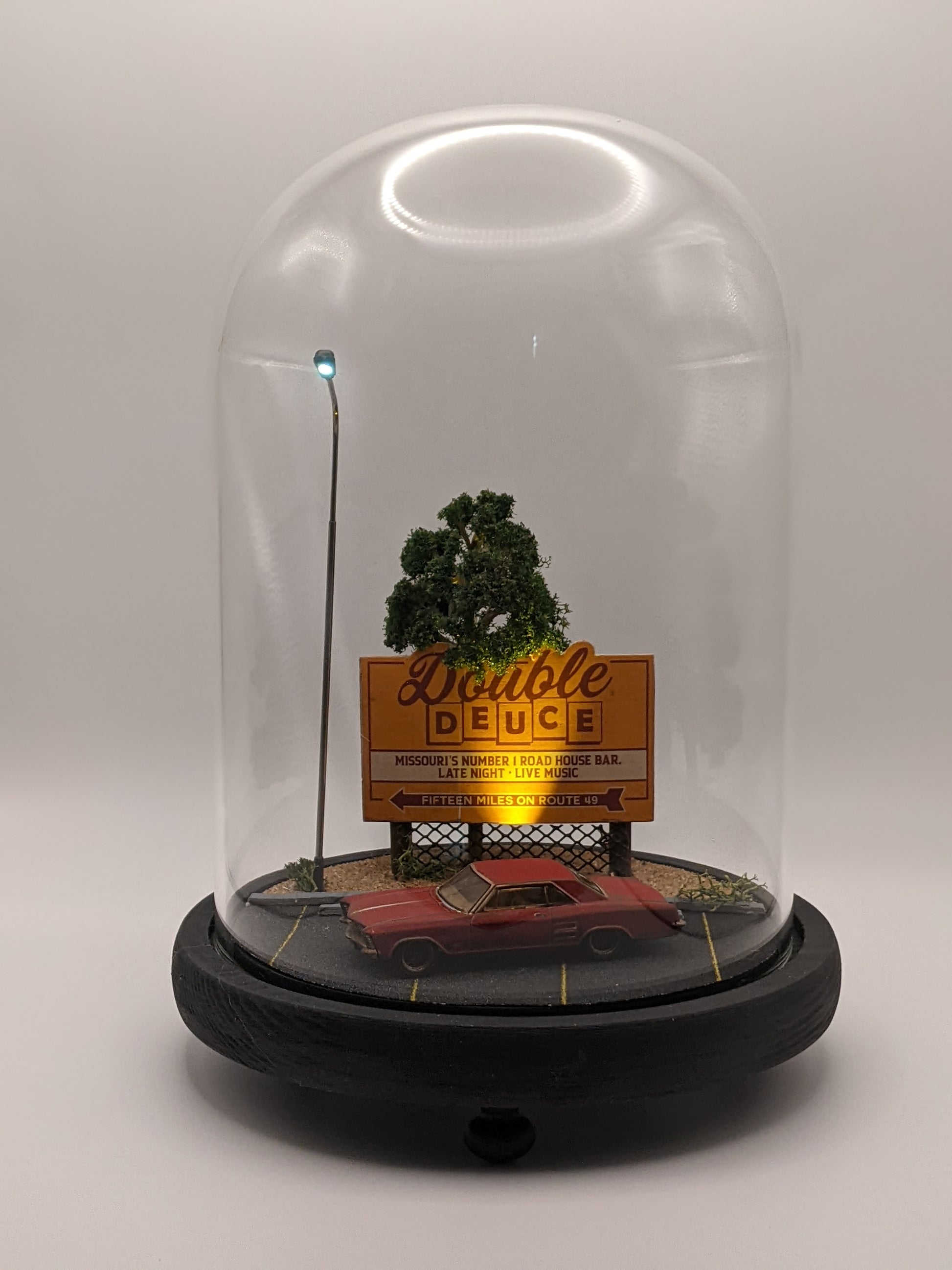 Model of a red car and tree under a glass dome with 'Double Deuce' sign.