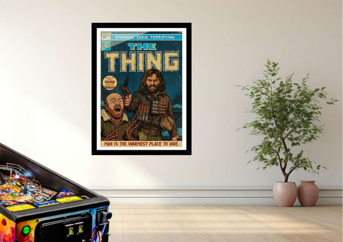 Framed comic book-style poster of 'The Thing' on a wall with a pinball machine and plants in the foreground.